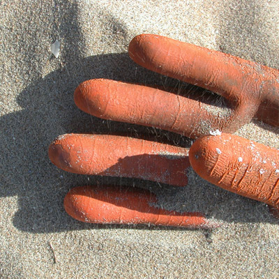 Naast de bank ligt een werkhandschoen half begraven in het zand, de rubberen vingers steken als oranje wortels uit het zand.