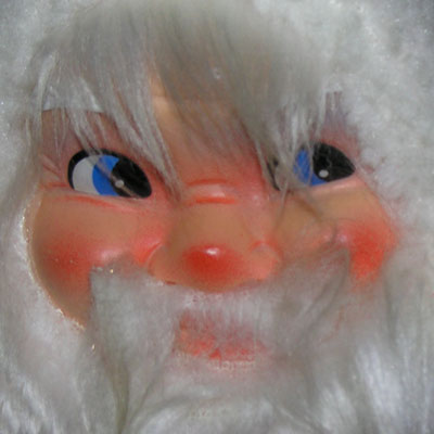 Op het tafeltje staat een kerstmannetje met een lelijk, glanzend gezichtje omringd door een krans van wit haar dat over gaat in een wit baardje